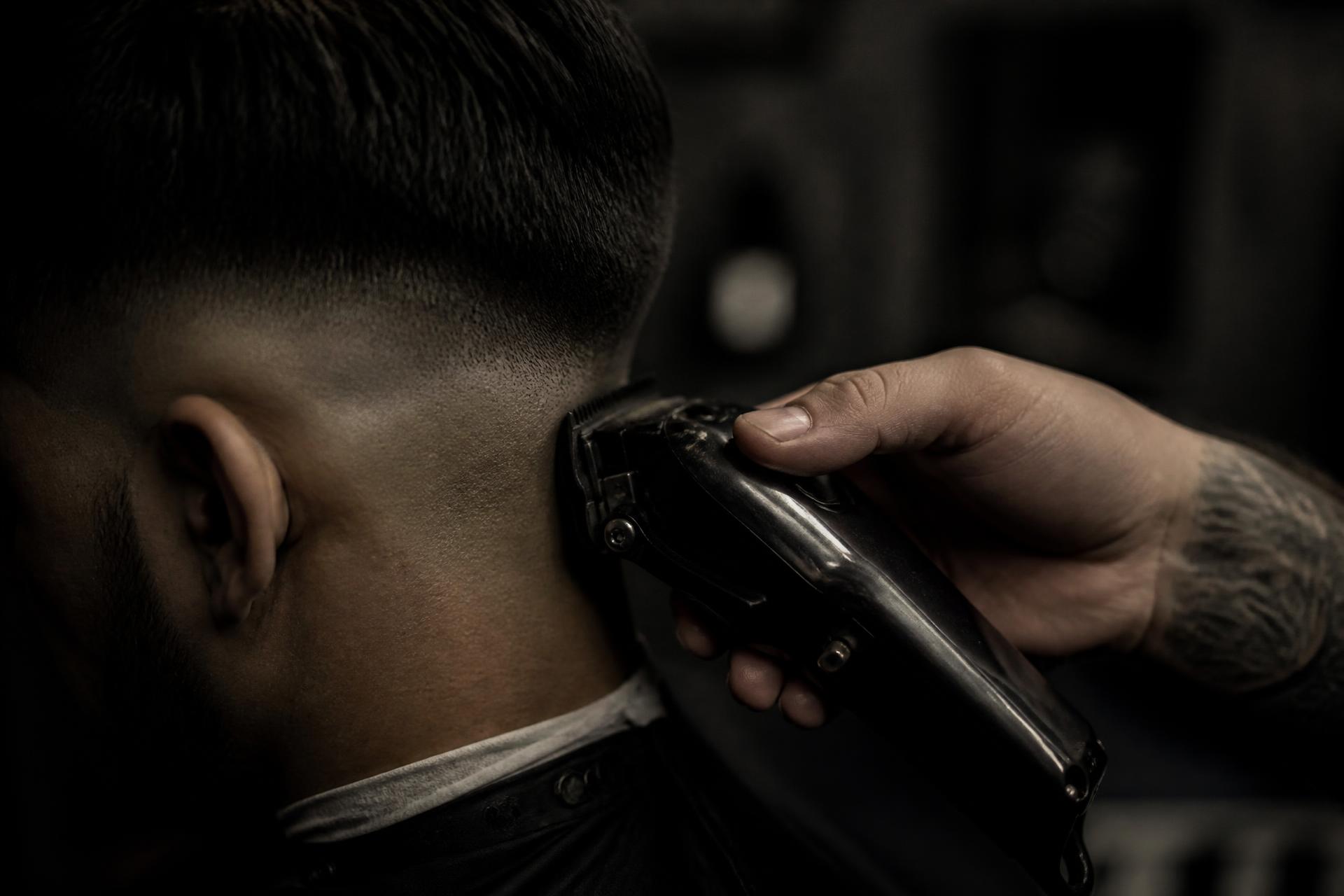 Barber using clippers to shape a fade in low, moody light